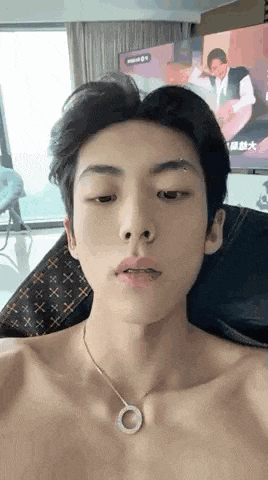 a shirtless young man wearing a necklace is sitting in a chair .