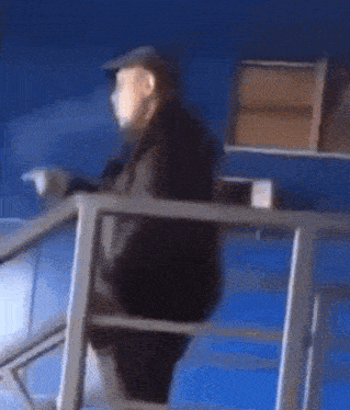 a man in a hat is walking down stairs with a blue wall in the background