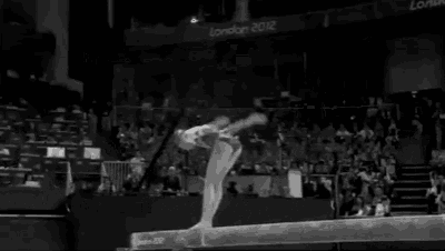a gymnast is doing a trick on a balance beam in front of a crowd .