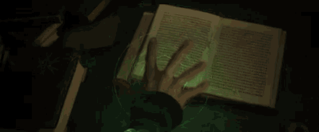 a person is casting a spell on a book with a green light coming out of their hand .