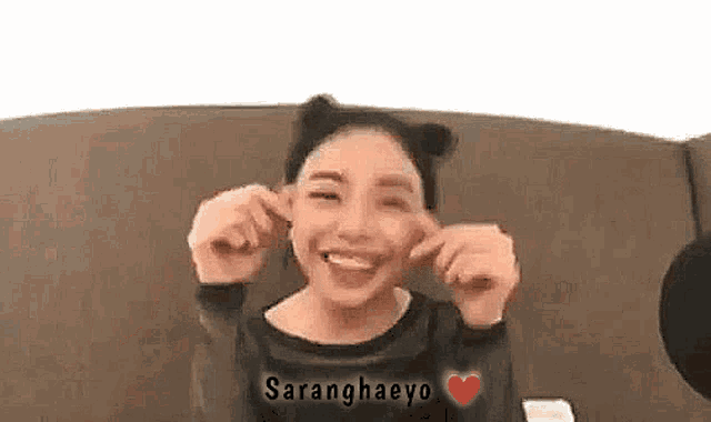 a woman is sitting on a couch with her hands in her ears and making a funny face .