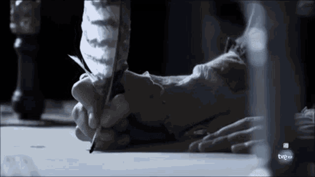 a close up of a person writing with a feather pen with the tv8 logo in the corner