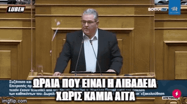 a man in a suit is giving a speech in front of a microphone in a greek language