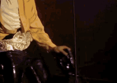 a man wearing a yellow shirt and black pants is standing in front of a microphone .