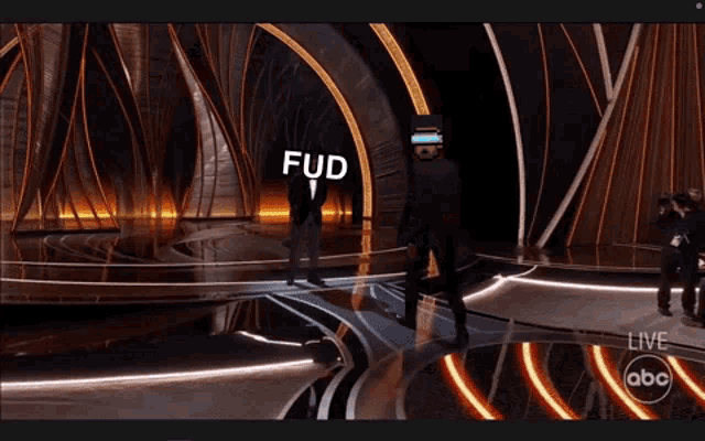 two men in tuxedos are dancing on a stage and one of them has the word fuc on his face