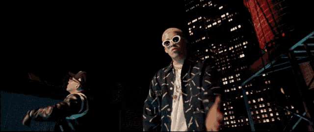 a man wearing sunglasses stands next to another man in front of a city skyline