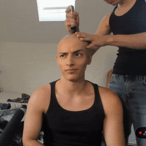 a man in a black tank top has his head shaved
