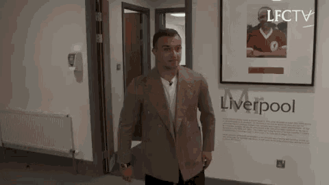 a man in a suit is standing in a hallway next to a framed picture of a man in a red shirt .
