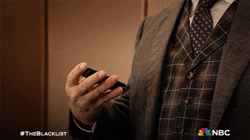 a man in a suit and tie is holding a cell phone with a nbc logo in the corner