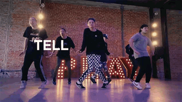 a group of young men are dancing in front of a brick wall with the words tell above them