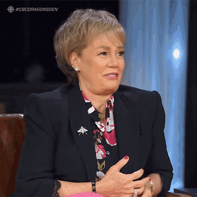a woman is sitting in a chair with her hands folded in front of a cbs dragonsden logo