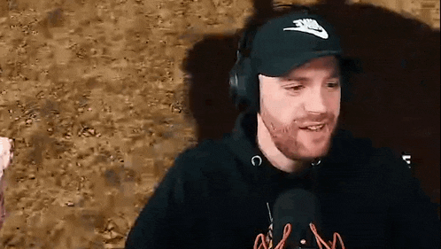 a man with a beard is wearing headphones and a hat while talking into a microphone .