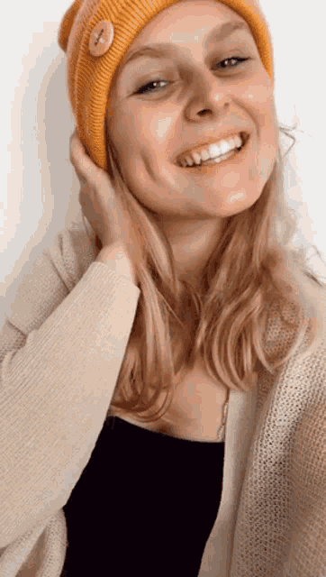 a woman wearing a yellow beanie with a button on it smiles