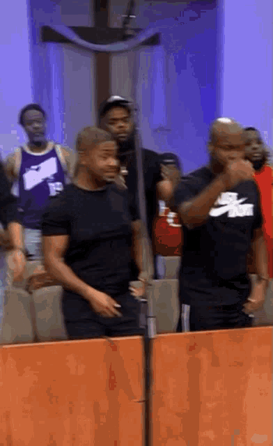 a group of men are standing in front of a microphone in a church . one of the men is wearing a nike shirt .