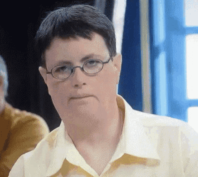 a man wearing glasses and a yellow shirt is making a funny face
