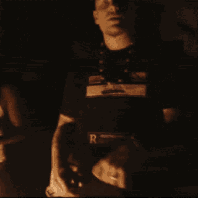 a man wearing a shirt with the letter r on it is standing in front of a fire