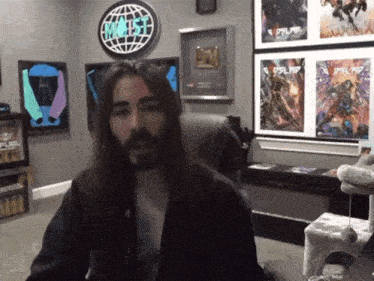 a man with long hair and a beard is sitting in front of a sign that says " most "