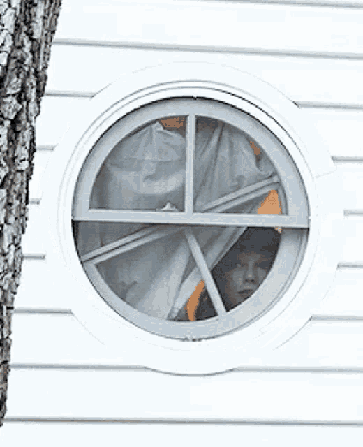 a round window on a white house with a person looking out