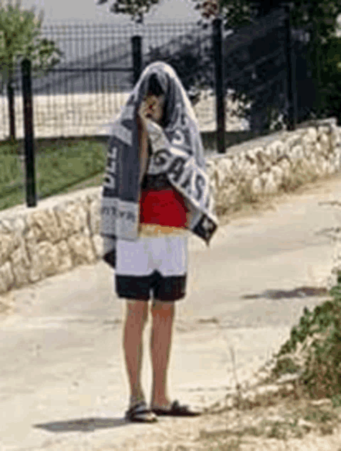 a person is standing on a sidewalk with a towel covering their face .