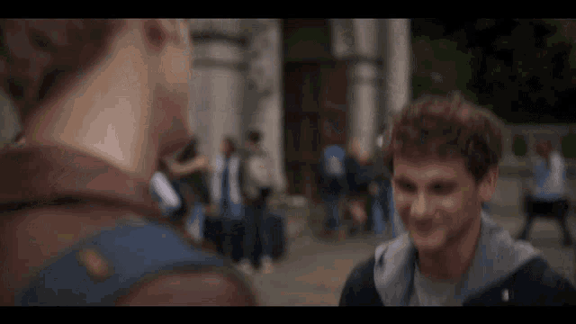 a man in a leather jacket talks to another man in a pink shirt