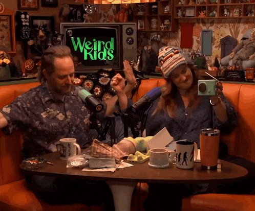 a man and a woman are sitting at a table in front of a weird kids sign