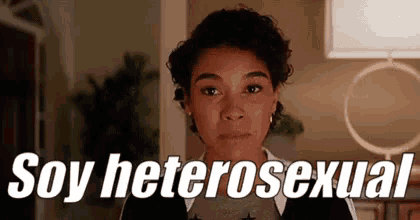 a young woman is standing in a living room with the words `` soy heterosexual '' written on the screen .