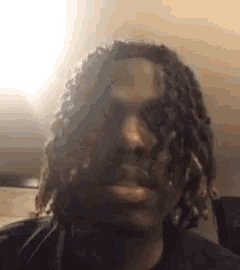 a young man with dreadlocks is smoking a cigarette in front of his face .