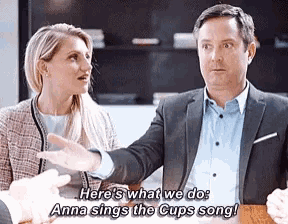 a man and a woman are sitting at a table and the man says here 's what we do anna sings the cup song