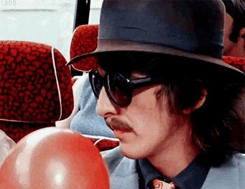 a man wearing a hat and sunglasses is blowing a red balloon .