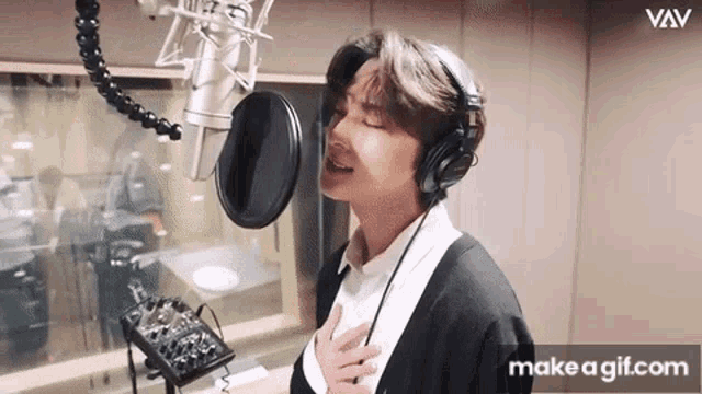 a young man wearing headphones is singing into a microphone in a recording studio .