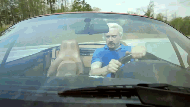 a man in a blue shirt is driving a convertible car