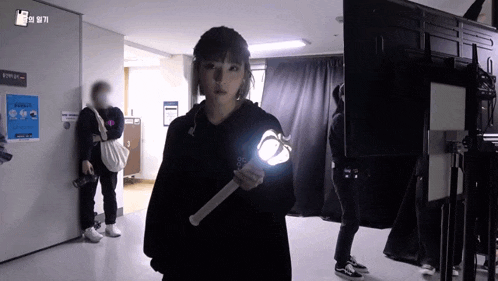 a woman in a black hoodie is holding a light in a dark room .