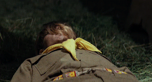 a boy scout with a yellow scarf around his neck is laying on the grass .
