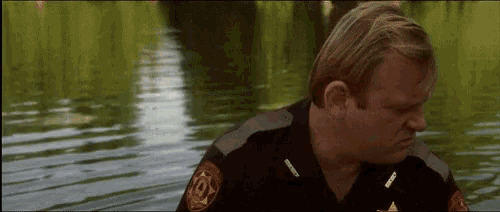 a man in a sheriff 's uniform is standing in a body of water .
