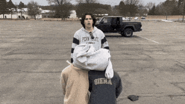 a man wearing a penn state sweatshirt stands in a parking lot