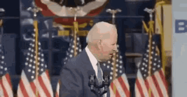 a man in a suit and tie is standing in front of a microphone in front of a wall of american flags .