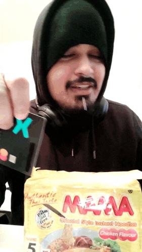 a man holding a credit card and a bag of mama instant noodles chicken flavour