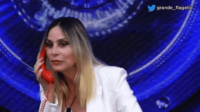 a woman in a white jacket is talking on a red telephone in front of a blue background with the hashtag grande flagello