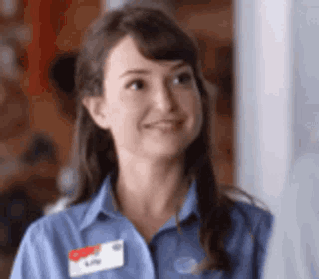 a woman in a blue shirt with a name tag on her shoulder is smiling .
