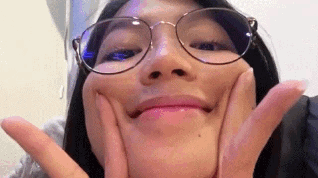 a woman wearing glasses is making a face with her hands .