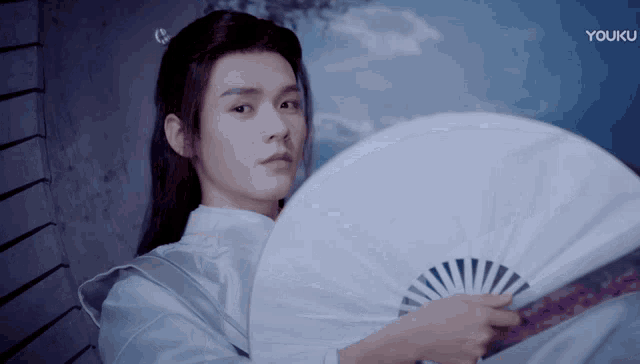 a man is holding a fan in front of a youku logo