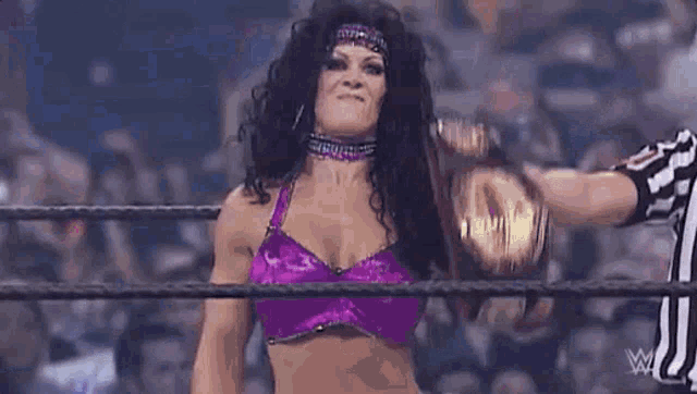a woman in a purple top is holding a wrestling championship belt .