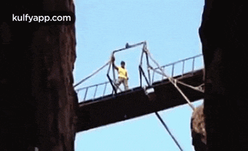 a man in a yellow shirt is standing on a bridge .