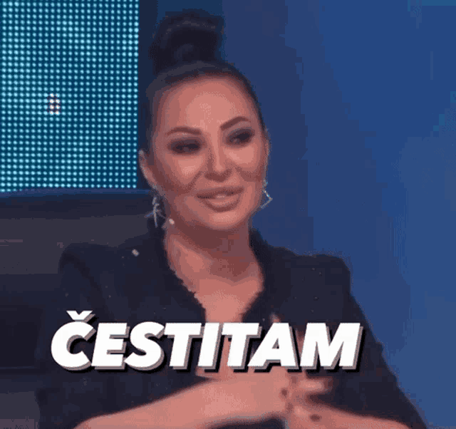 a woman in a black jacket is sitting in front of a screen that says ' cestitam ' on it .