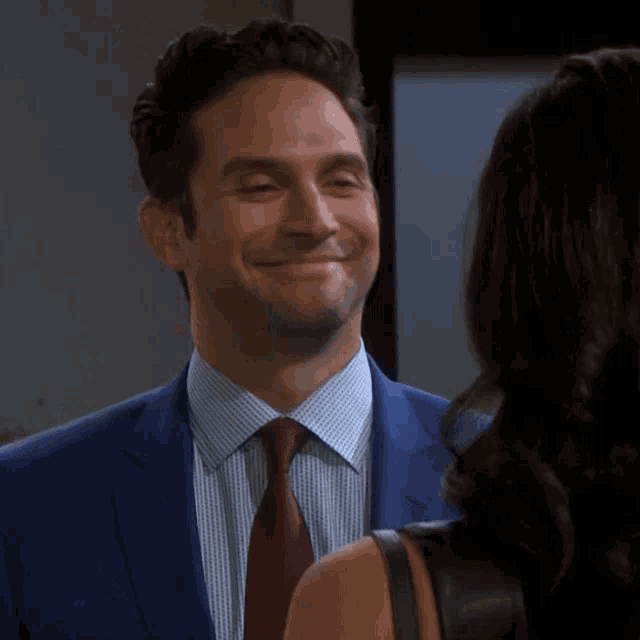 a man in a suit and tie smiles while looking at a woman