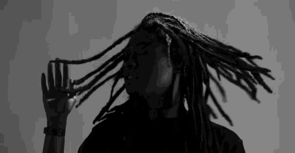 a black and white photo of a woman with dreadlocks holding her hair .