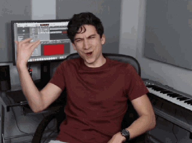 a man in a red shirt is sitting in front of a keyboard and computer