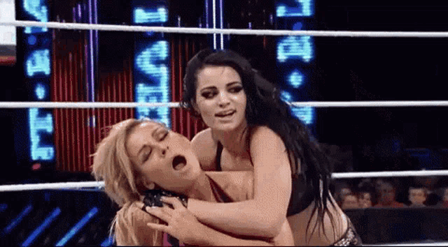 two women are wrestling in a wrestling ring and one of them is holding the other 's arm .
