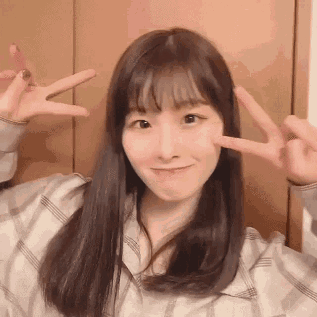 a young woman with long hair is making a peace sign with her fingers .