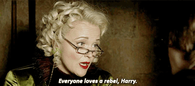 a woman wearing glasses and a green jacket says " everyone loves a rebel harry "